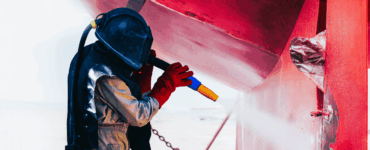 Worker sandblasting corroded hull boat